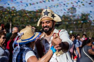 Um homem vestindo roupas típicas da Festa Junina (festa junina), dançando, tocando música e sorrindo